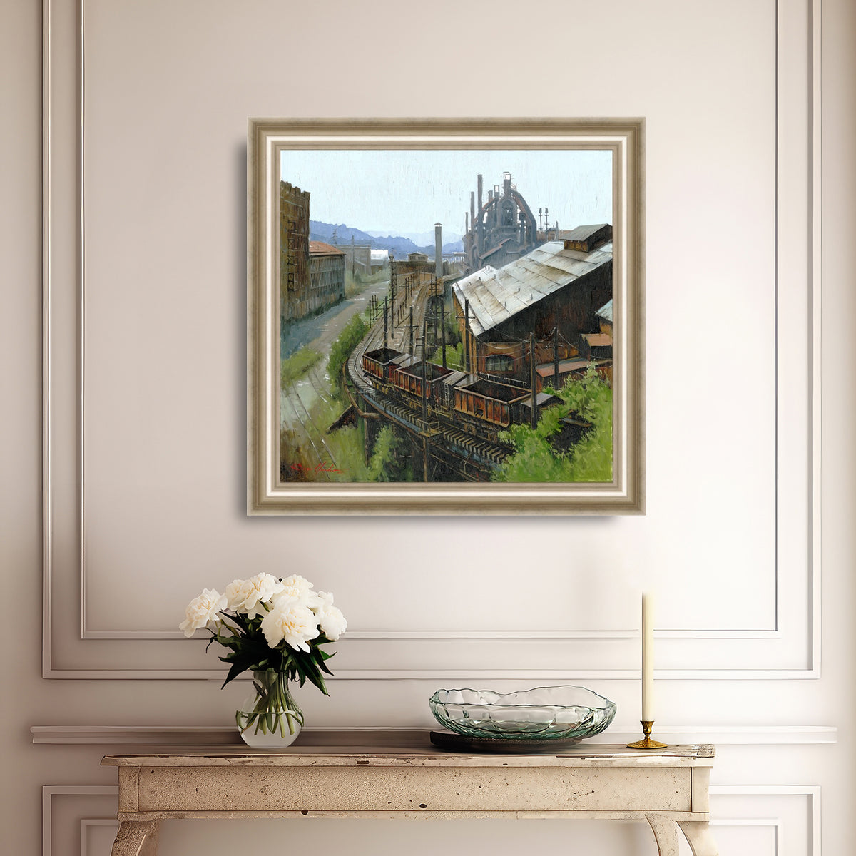 Framed painting of an industrial scene on a wall above a console table with decorative items.