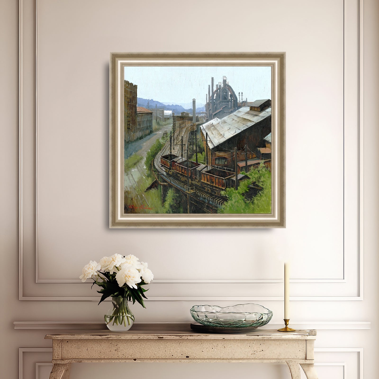 Framed painting of an industrial scene on a wall above a console table with decorative items.