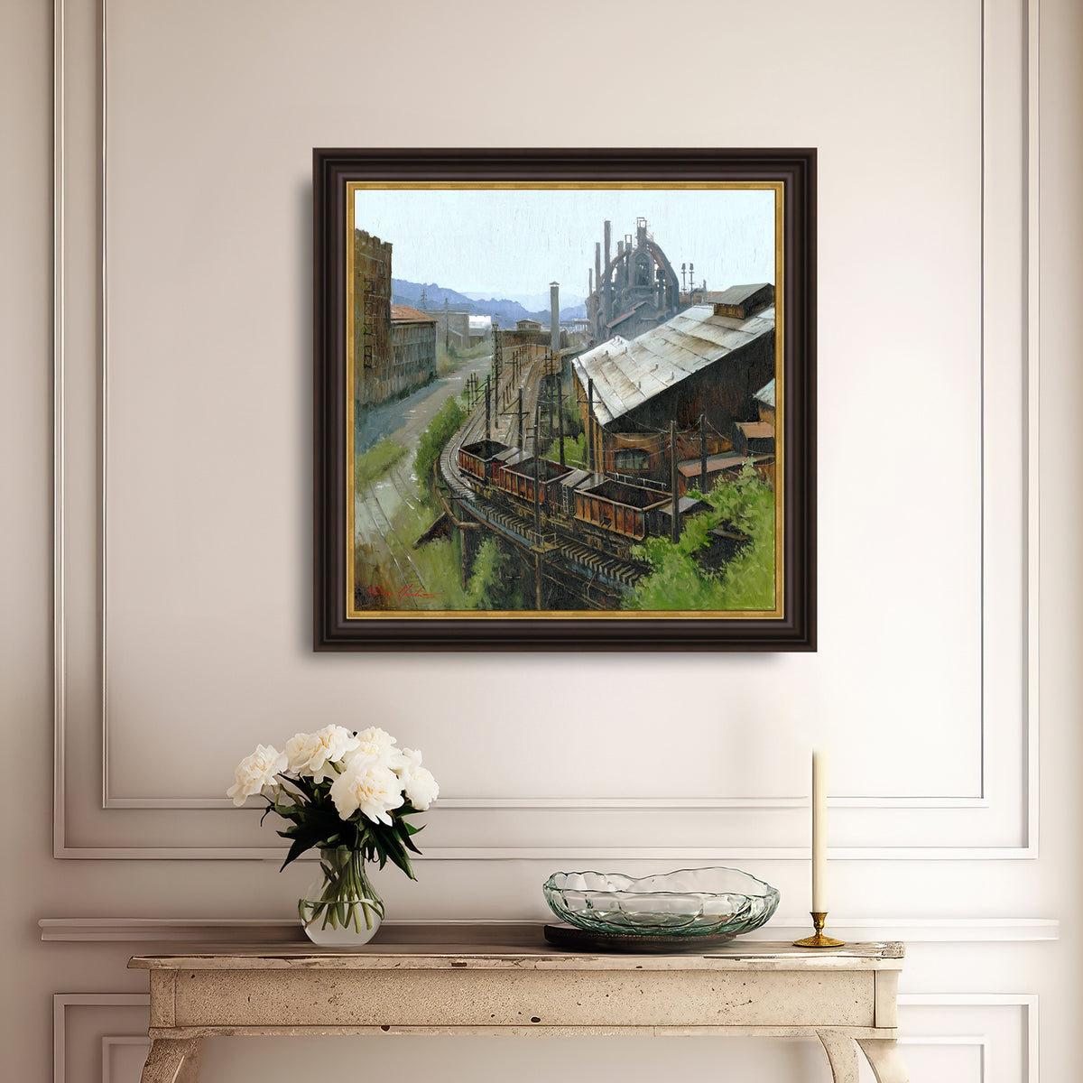 Framed painting of an industrial scene on a wall above a console table with decorative items.