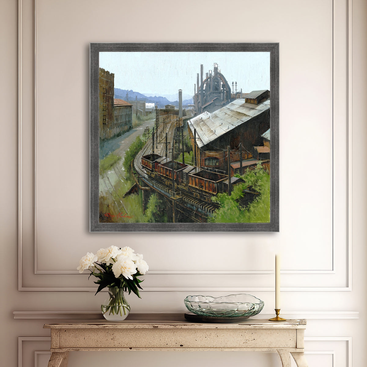 Framed industrial scene painting on a wall above a console table with decorative items.