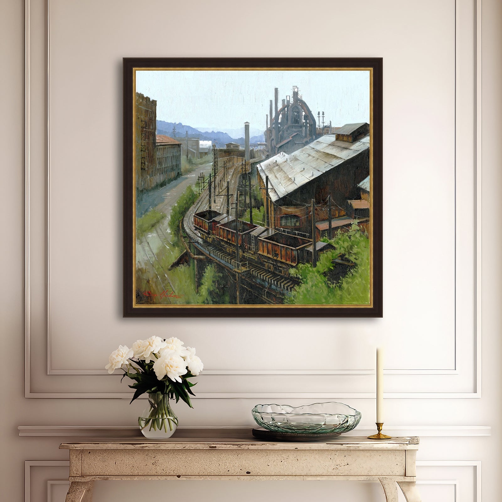 Framed painting of an industrial scene on a wall above a console table with decorative items.