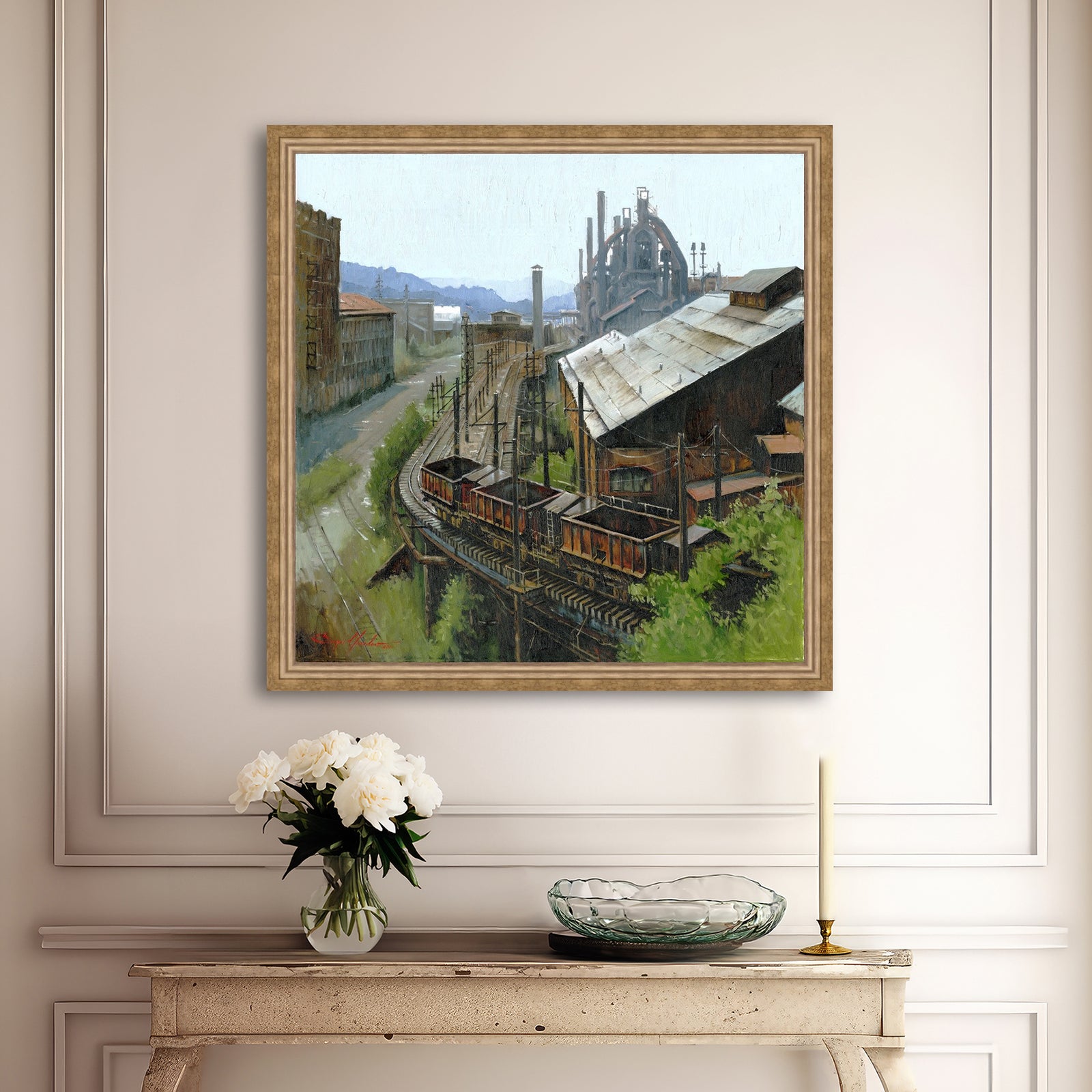 Framed industrial landscape painting on a wall above a console table with decorative items.