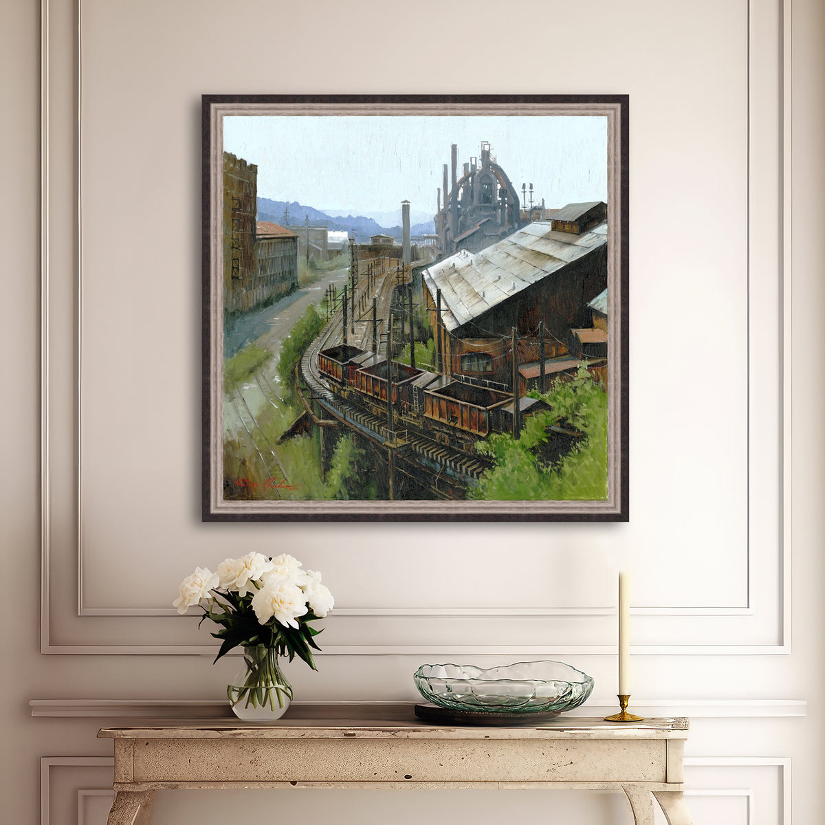 Framed industrial scene painting on a wall above a console table with decorative items.