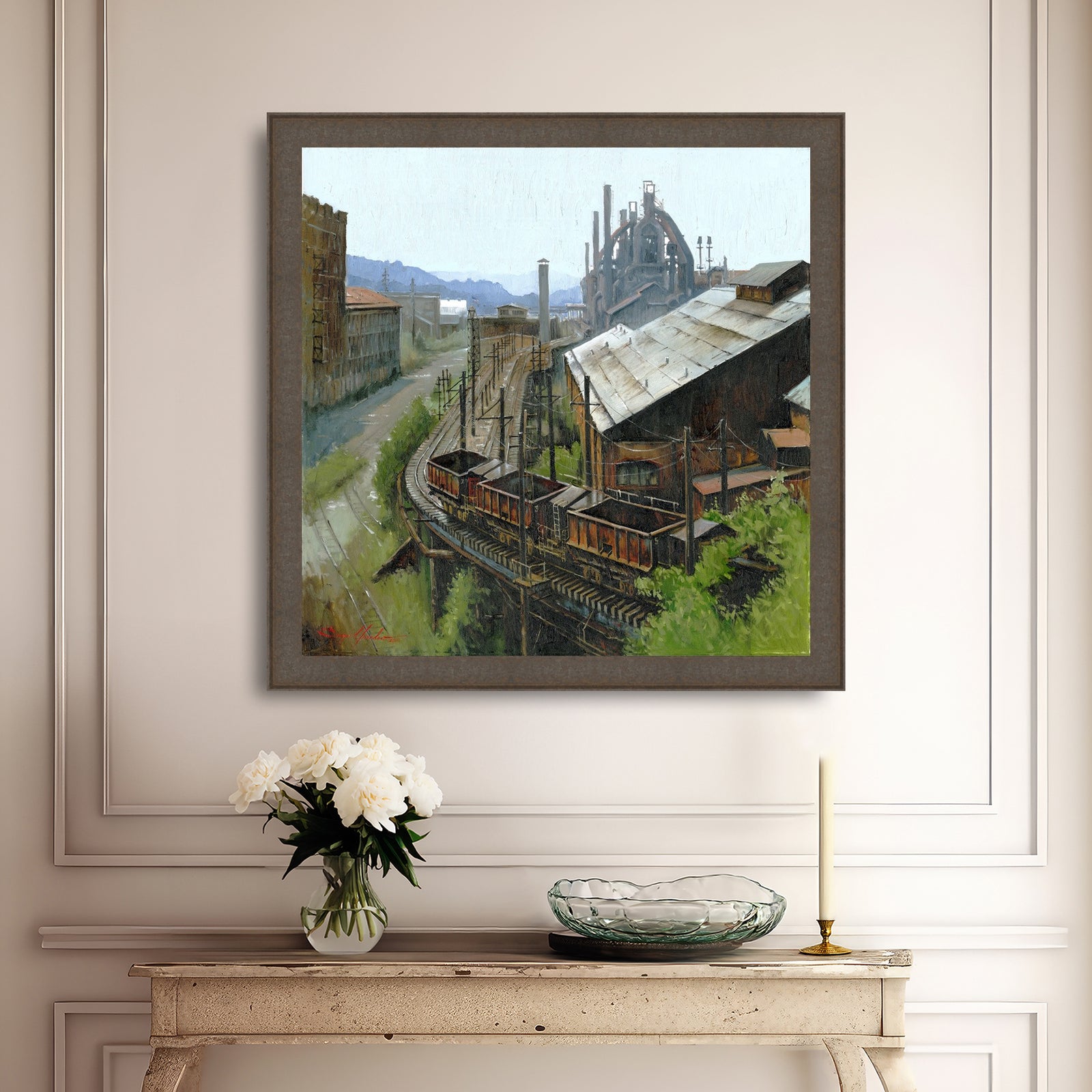 Framed painting of an industrial scene on a wall above a console table with decorative items.